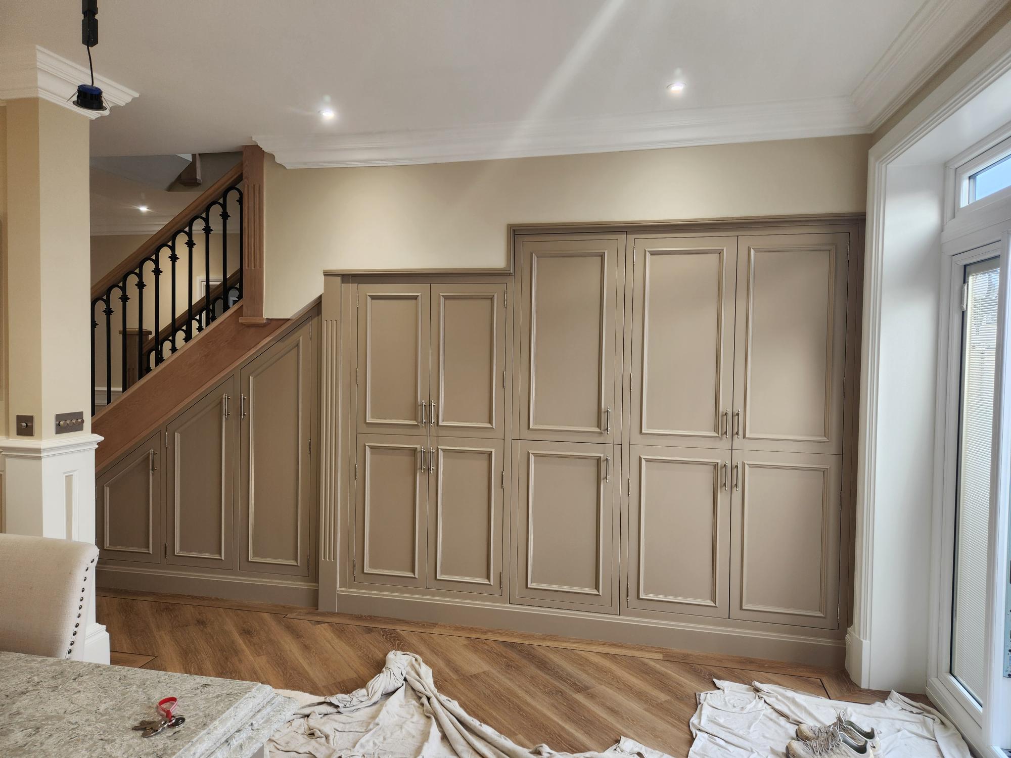 Full-wall fitted storage cupboards in taupe with under-stairs integration