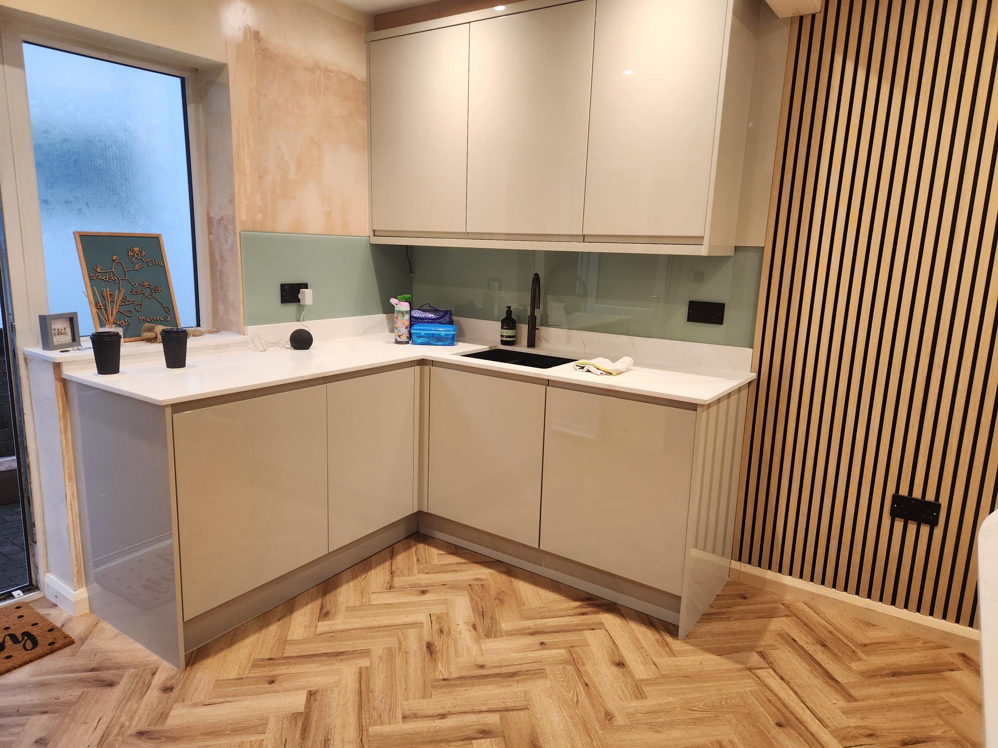 Compact L-shaped kitchen with sage glass splashback and wood slat wall