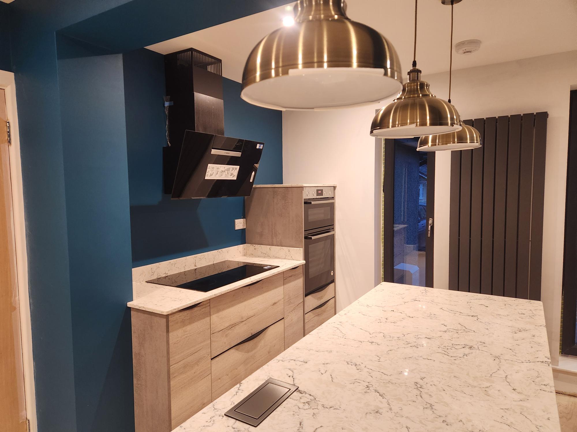 Kitchen with wood-effect units, teal walls and brass pendant lights
