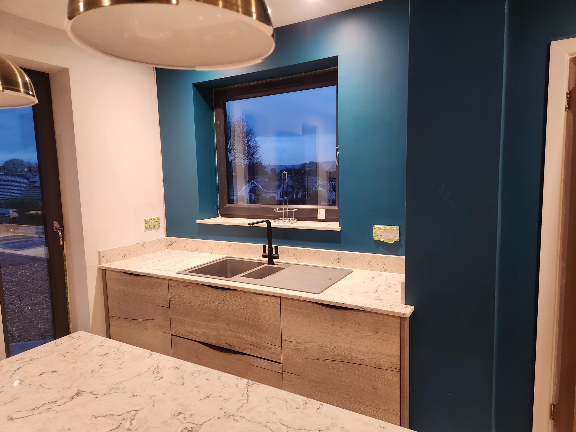 Kitchen sink run with marble worktop and teal feature wall