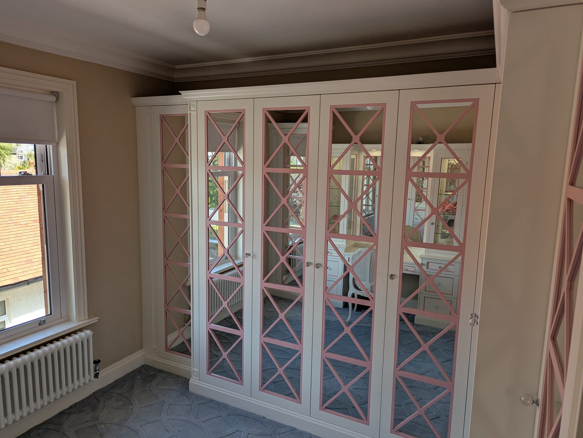 Fitted wardrobes with pink criss-cross pattern mirrored doors